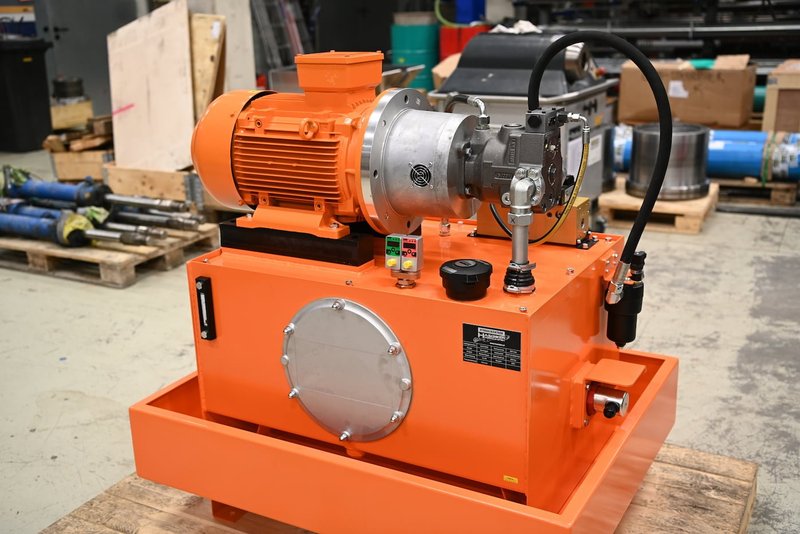 Orangefarbenes Hydraulikaggregat mit Elektromotor und Pumpe auf Palette in der Werkstatt