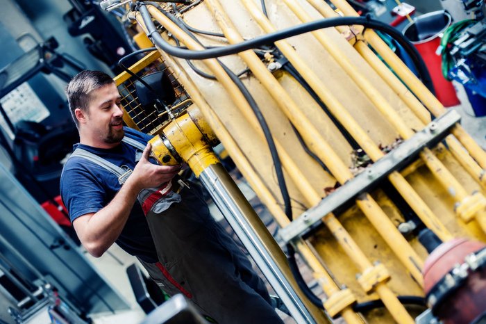 Mitarbeiter überprüft ein Hydrauliksystem an einer gelben Maschine in der Werkstatt